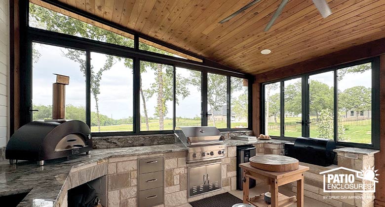 An outdoor kitchen with pizza oven, grill and smoker, enclosed with glass for protection from dirt, dust and rain..