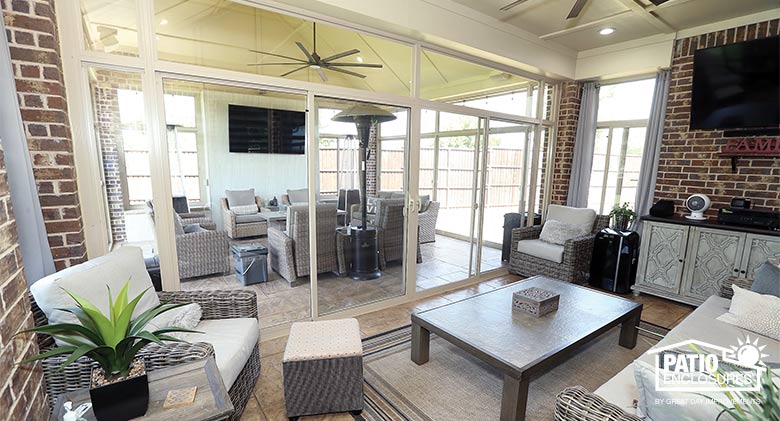 A glass Florida room leads out to a screen room, both comfortably furnished with cushioned chairs, sofa and televisions.