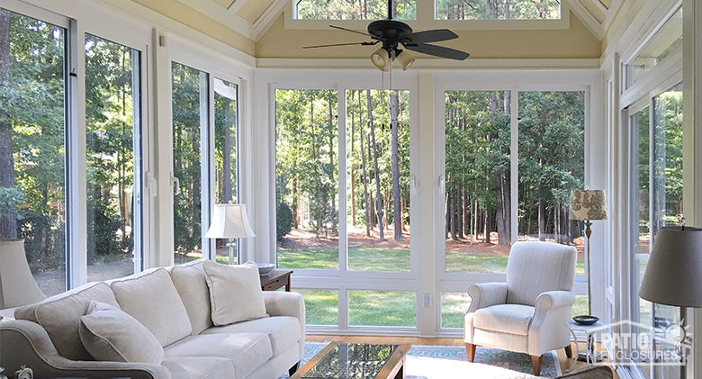 The interior of a white-framed sunroom with ceiling fan, upholstered furniture, coffee table and various lamps.
