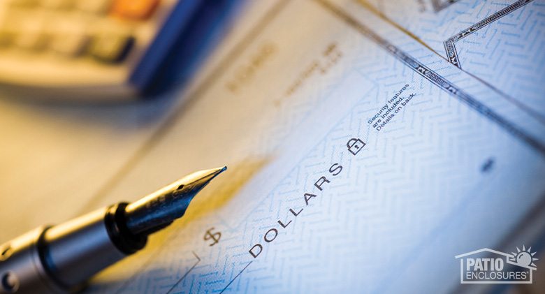 Closeup of a blank check with a pen laying on top and a blurry calculator in the background.