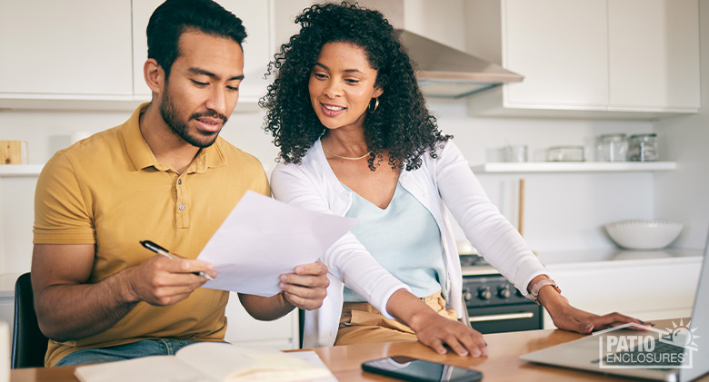 Couple sitting at kitchen counter with laptop and phone reviewing their budget.