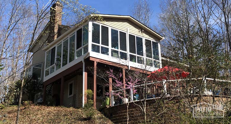 Looking uphill at a large sunroom on the second floor of a home in the woods with stairs in the foreground.