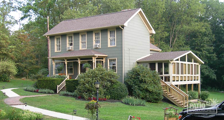 A colonial home on a slight hill with a sunroom on the right side, stairs coming down from the sunroom.