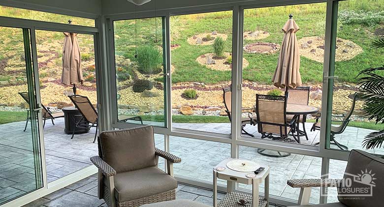 The interior of a sunroom looking out to the patio area with tables and chairs. The land rises dramatically beyond the patio.