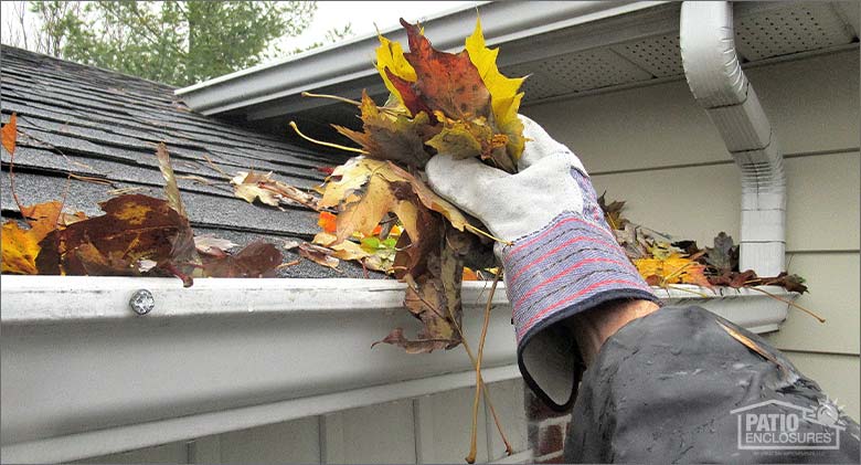 Image of a hand with a work glove pulling dead leaves from a clogged gutter.