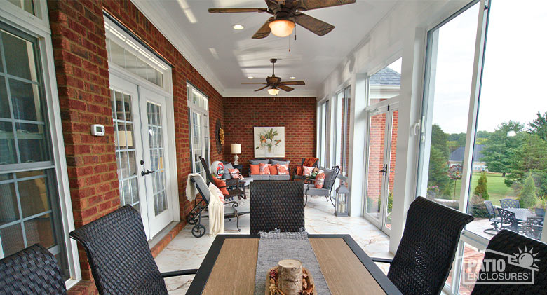 A table and chairs in the foreground and a seating area in the background of a long, narrow glass three-season room.