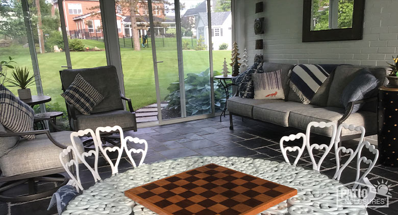 A table with a checkerboard in the foreground and comfortable gray furniture in the background of a three-season sunroom.