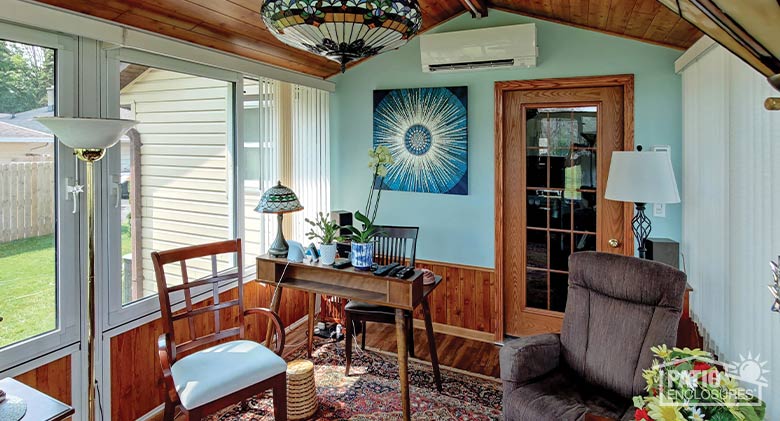 : Home office with a desk and side chairs in a four-season sunroom with wood-paneled knee wall, oriental rug & vertical blinds.
