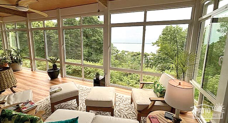 : Home office with a desk and side chairs in a four-season sunroom with wood-paneled knee wall, oriental rug & vertical blinds.