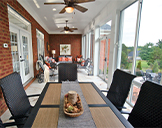 A table and chairs in the foreground and a seating area in the background of a long, narrow glass three-season room.