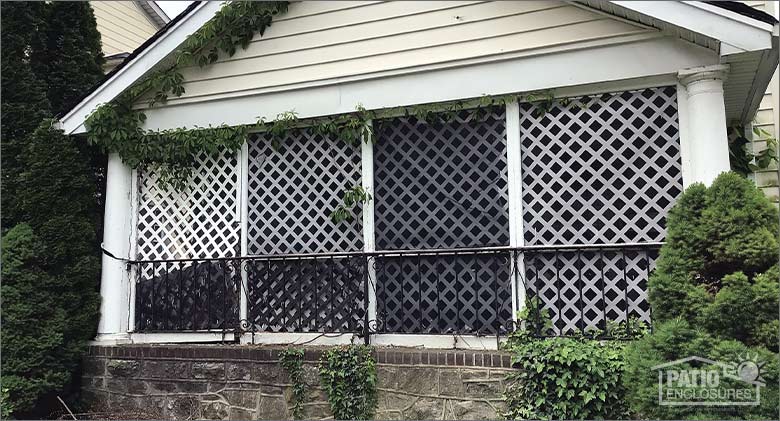 An old screen room in disrepair with torn screens, ivy growing into the room and a broken railing.