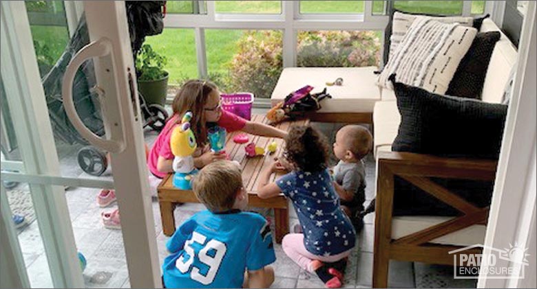 A group of young children playing with toys on a coffee table in a sunroom with sofa and ottoman.