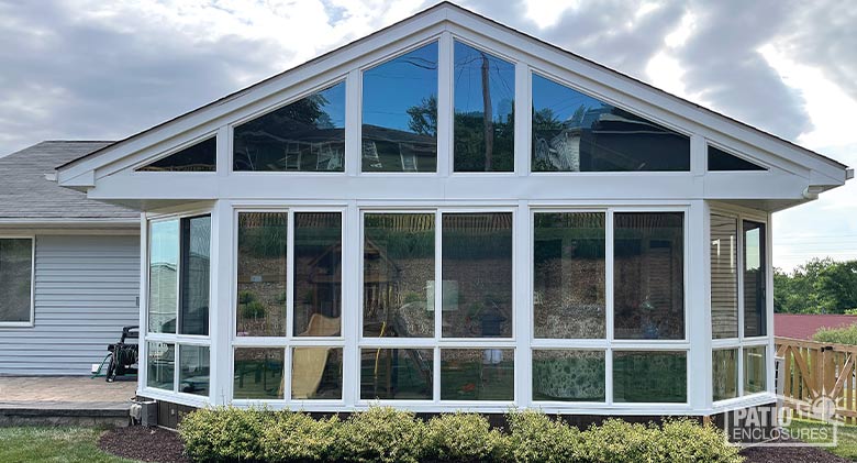 Exterior of a white glass three-season sunroom with shingled gable roof, glass wings and glass knee wall.