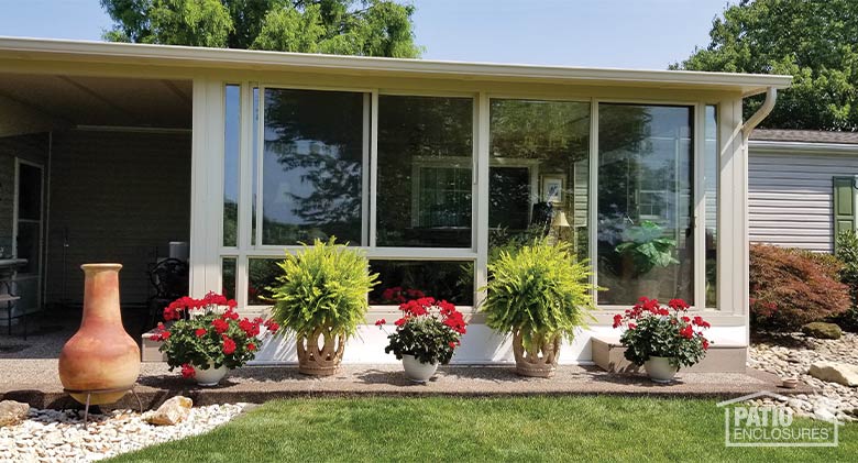 Beige three-season glass sunroom exterior with potted plants and flowers in front.
