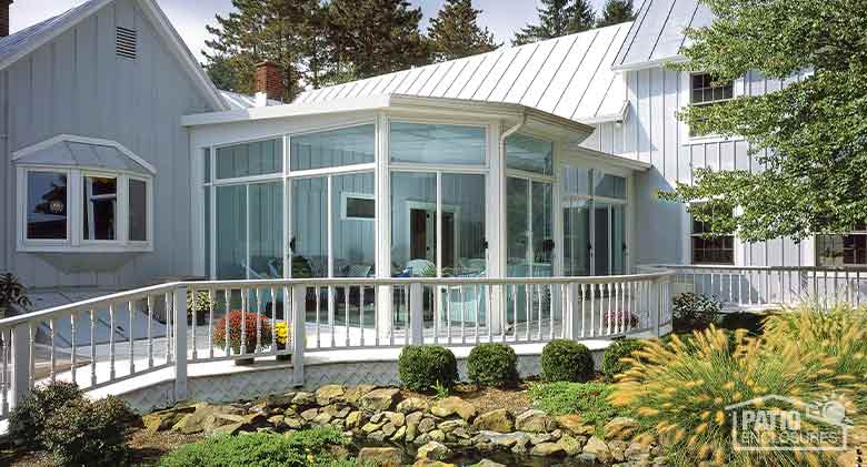 White four-season sunroom with aluminum frame, glass knee walls, gable roof and stone fascia.