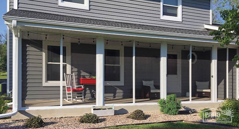 Screened patio enclosure on a gray house with neat plantings in front. Red cushion on rocker and two white chairs inside.