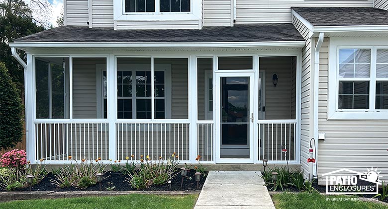 Tan home with screen-enclosed front porch with a picket railing. Neat plantings in front of the porch.
