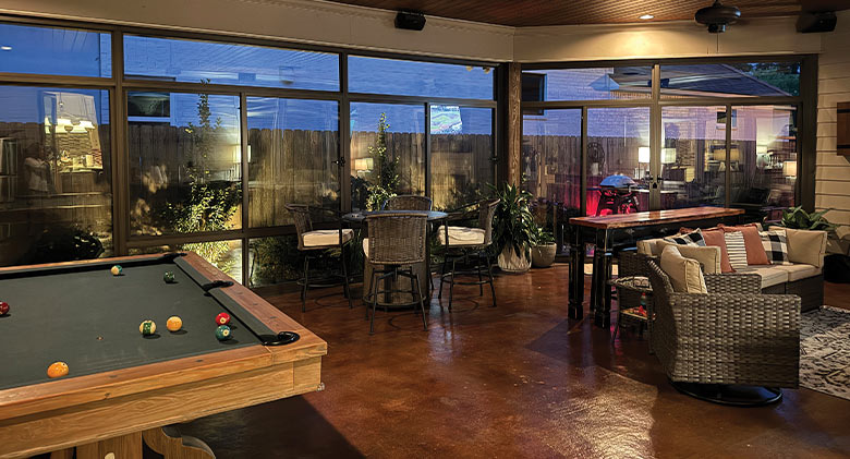 Interior of a glass patio enclosure at night with accent lighting highlighiting dining area, seating area, & billiard table.
.