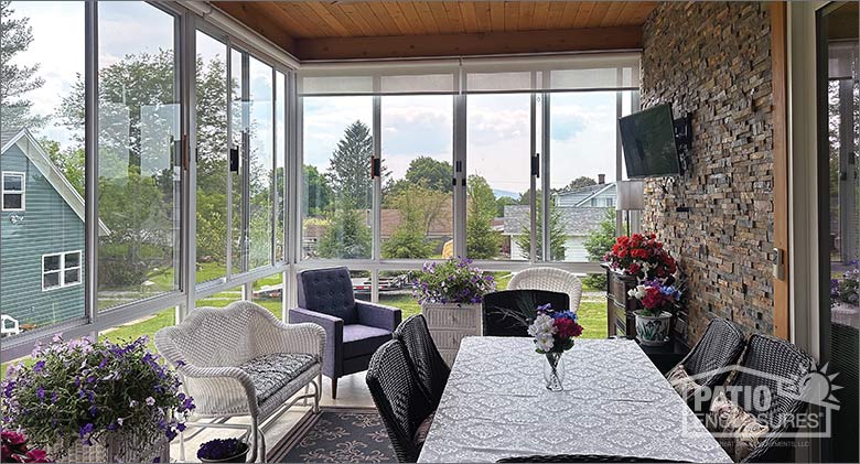 The interior of an upstairs sunroom with a dining table, comfortable seating area, and mounted television on a stone wall.