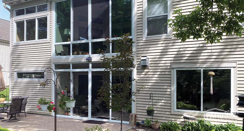 Looking up at a home on a hill with a gable-roofed sunroom on the second story. A large deck attaches to the sunroom.