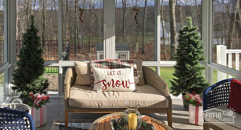 Sun streaming in through the windows of a sunroom lighting a loveseat with pillows and other holiday décor.