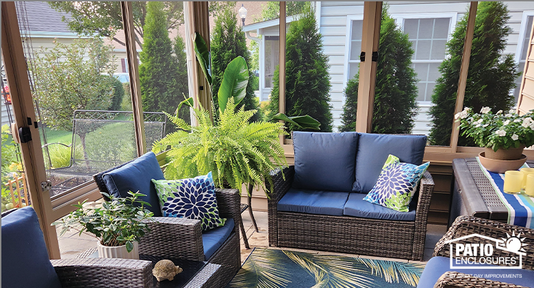 The interior of a Florida room with tan frame and furnished with brown wicker furniture with blue cushions and print pillows.