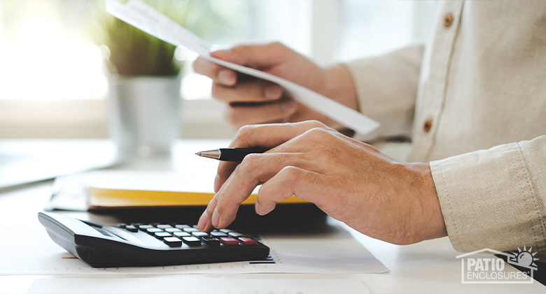 : A closeup of the hands of a man using a calculator and holding a pen and piece of paper.