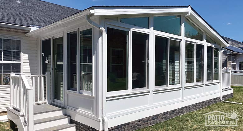 White three-season sunroom with gable roof and glass wings, solid knee wall and three steps leading up to sliding door..