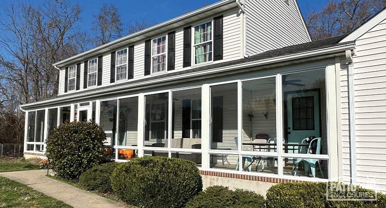 A white colonial home with a wide front porch enclosed in glass..