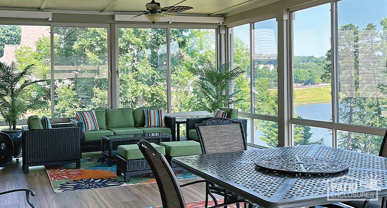 A glass sunroom enclosure overlooking a lake and furnished with seating area as well as a dining area.