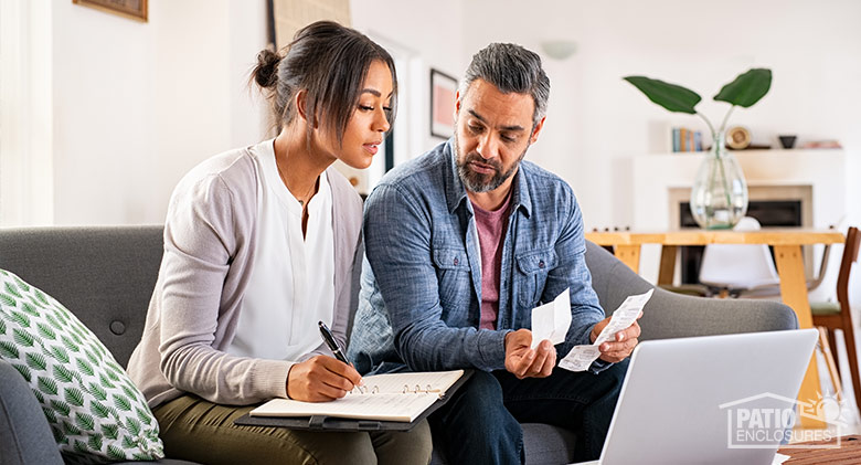 A couple looking at receipts and a laptop and making notes in a book to prepare a budget.