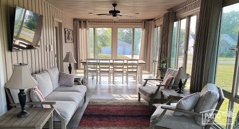 A glass-enclosed porch with a dining area in the back and a seating area with television in front.