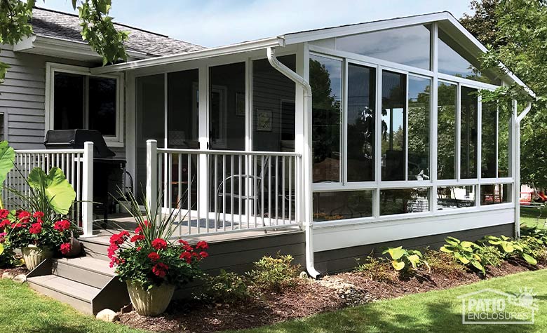 A large white gable-roofed sunroom with small deck and neat landscaping around including red potted flowers.