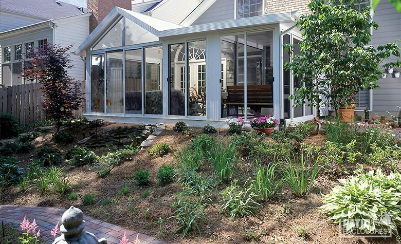 A walkway and hillside garden of grasses, flowers and small trees in front of a combination gable and shed-roofed sunroom.