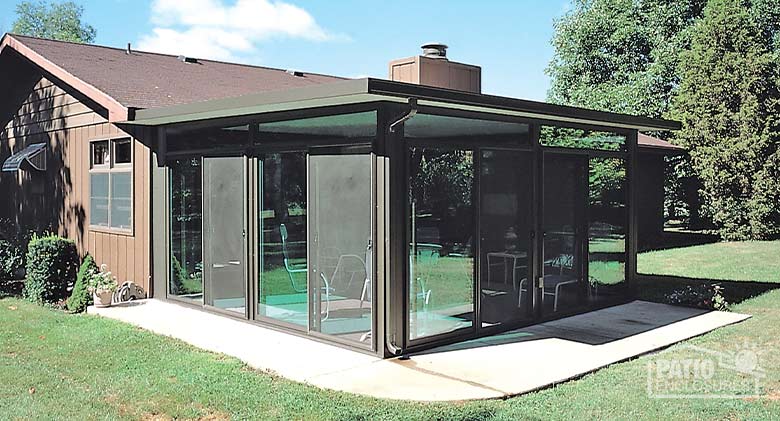 A brown glass sunroom enclosed a concrete patio in the backyard of a one-story home.
