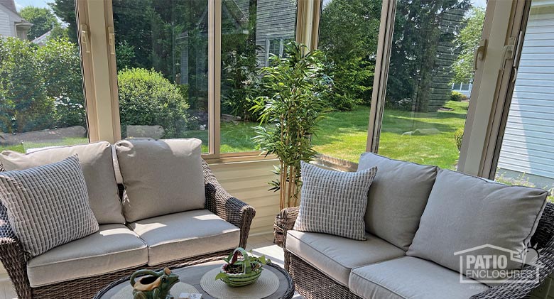 Close-up of the interior of a beige glass sunroom with two wicker loveseats with beige cushions.