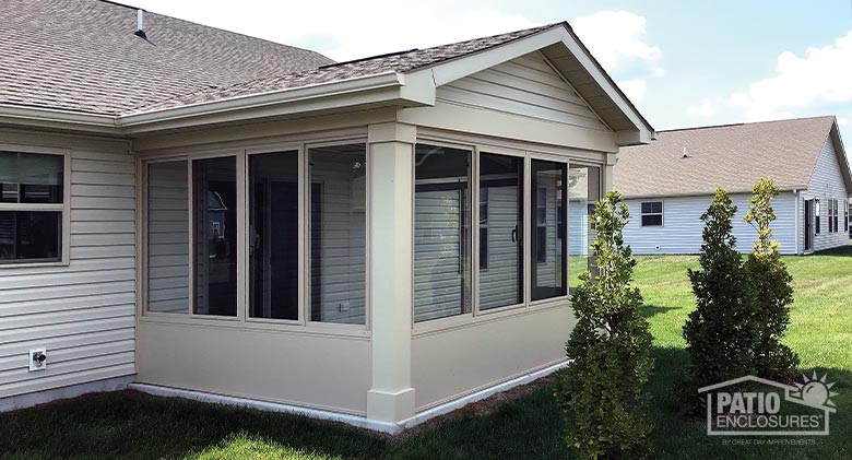 The exterior of a tan patio enclosure with solid knee walls and gable roof.