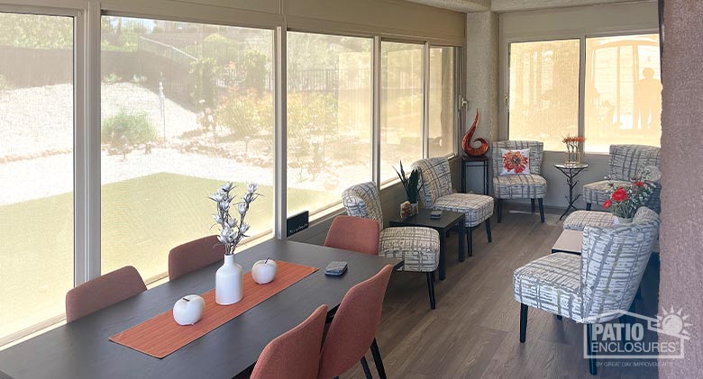 A glass patio enclosure with dining table and a large seating area.