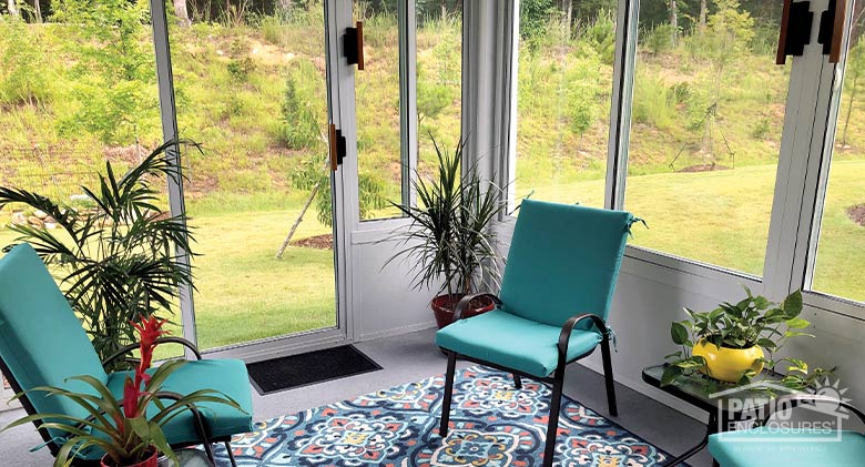 Potted plants and bright aqua chairs with matching print carpet furnish a glass three-season room.