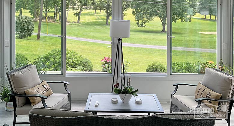 Two chairs, coffee table, and a lamp inside a white glass sunroom with solid knee wall.