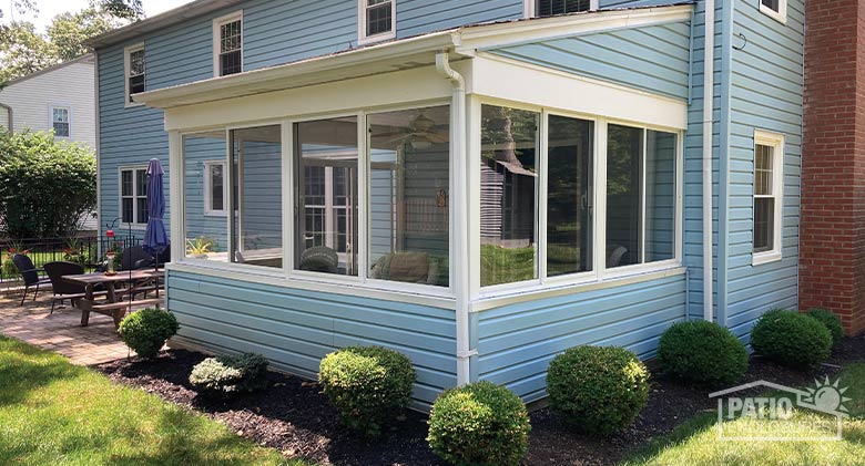 An covered patio on a blue-sided home is enclosed with glass for three season use.