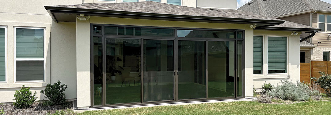 Custom under existing roof sunroom featuring floor-to-ceiling glass walls and sliding doors for year-round outdoor living.