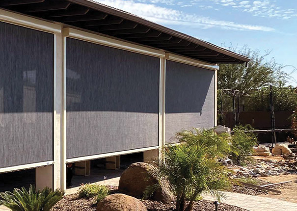 The exterior of a tan home with a covered patio protected by retractable screens, shown partially raised.
