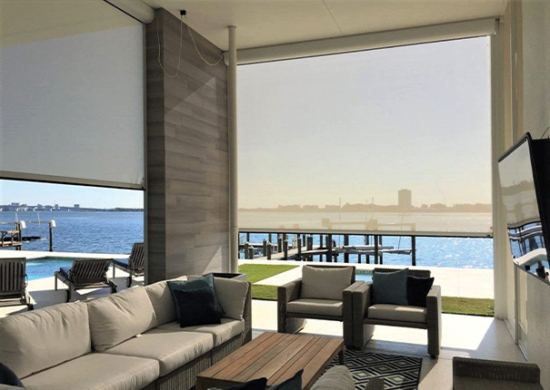 A comfortable seating area with TV in a covered patio. The openings are covred with beige opaque retractable screens.
