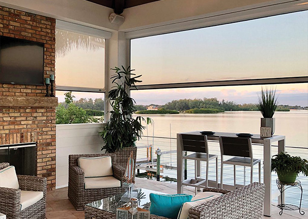 A fireplace and comfortable seating area in a covered patio shown with opaque retractable screens partially down.
