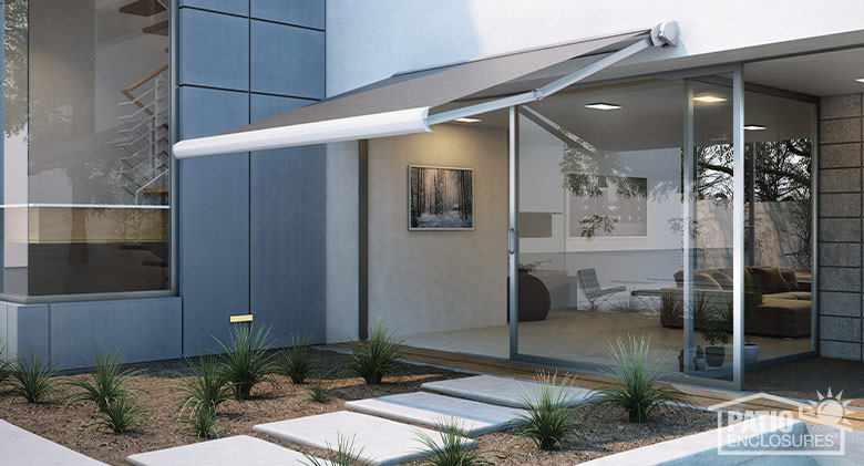 A gray and white retractable awning extended over a walkway leading to sliding doors on a contemporary home.