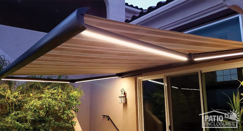 A striped retractable awning with illuminated light bars fully extended at a sliding door entry.