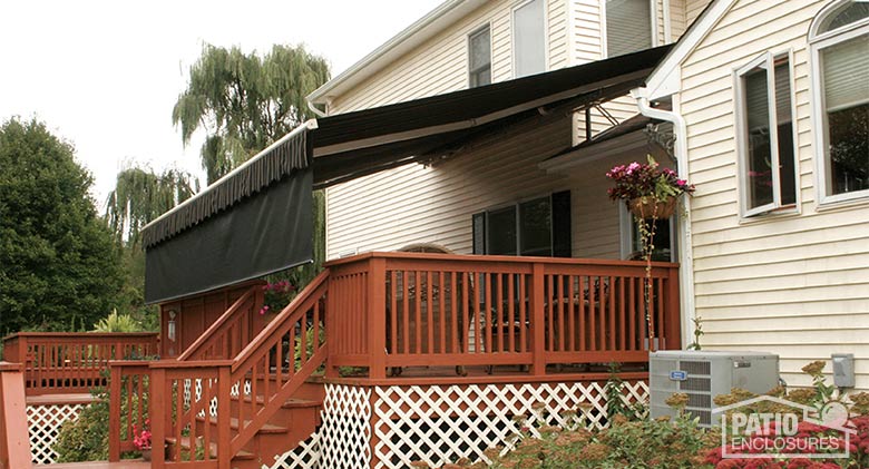  Dark brown retractable awning with drop valance covering a raised deck on a cream-colored home.