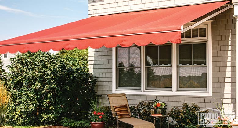 A bright orange retractable awning fully extended covers an outdoor patio with chaise lounge chair and potted plants.