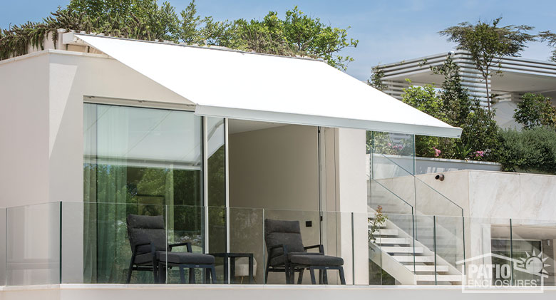 A flat white retractable awning covering a patio with two brown chairs and a table. Stairs on the right. 
